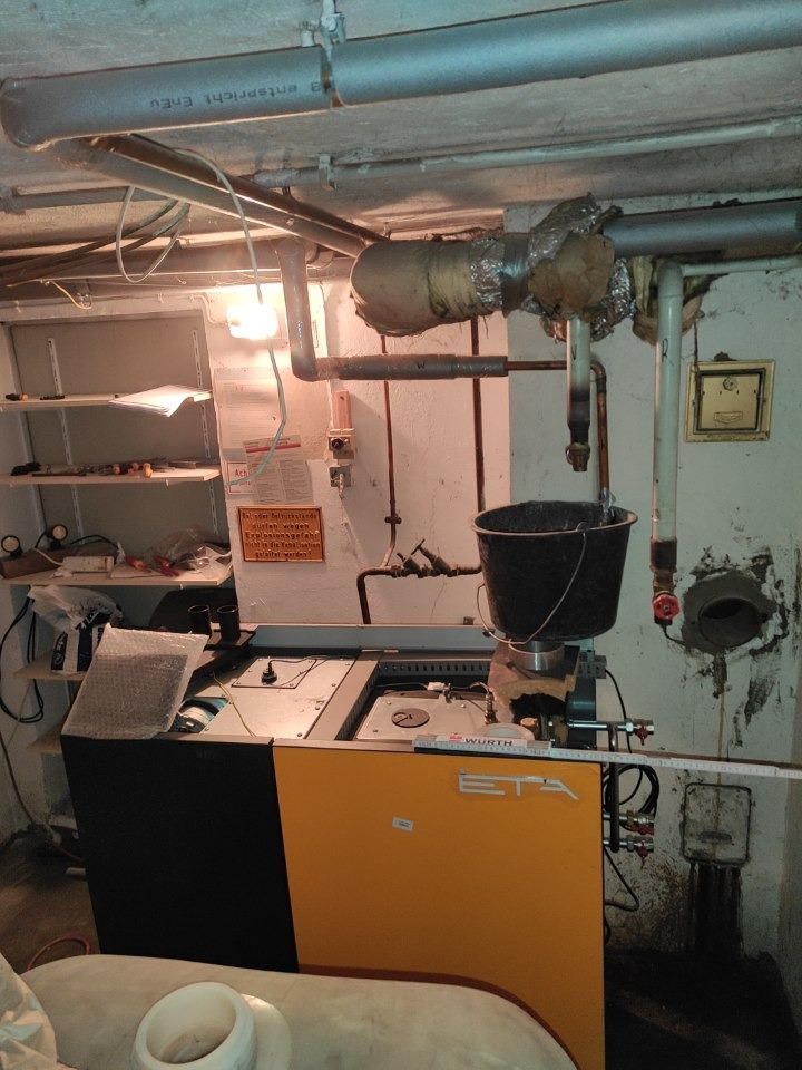 Kotłownia z piecem ETA, rurami i wiadrem zbierającym skropliny, widok na instalację w piwnicy.