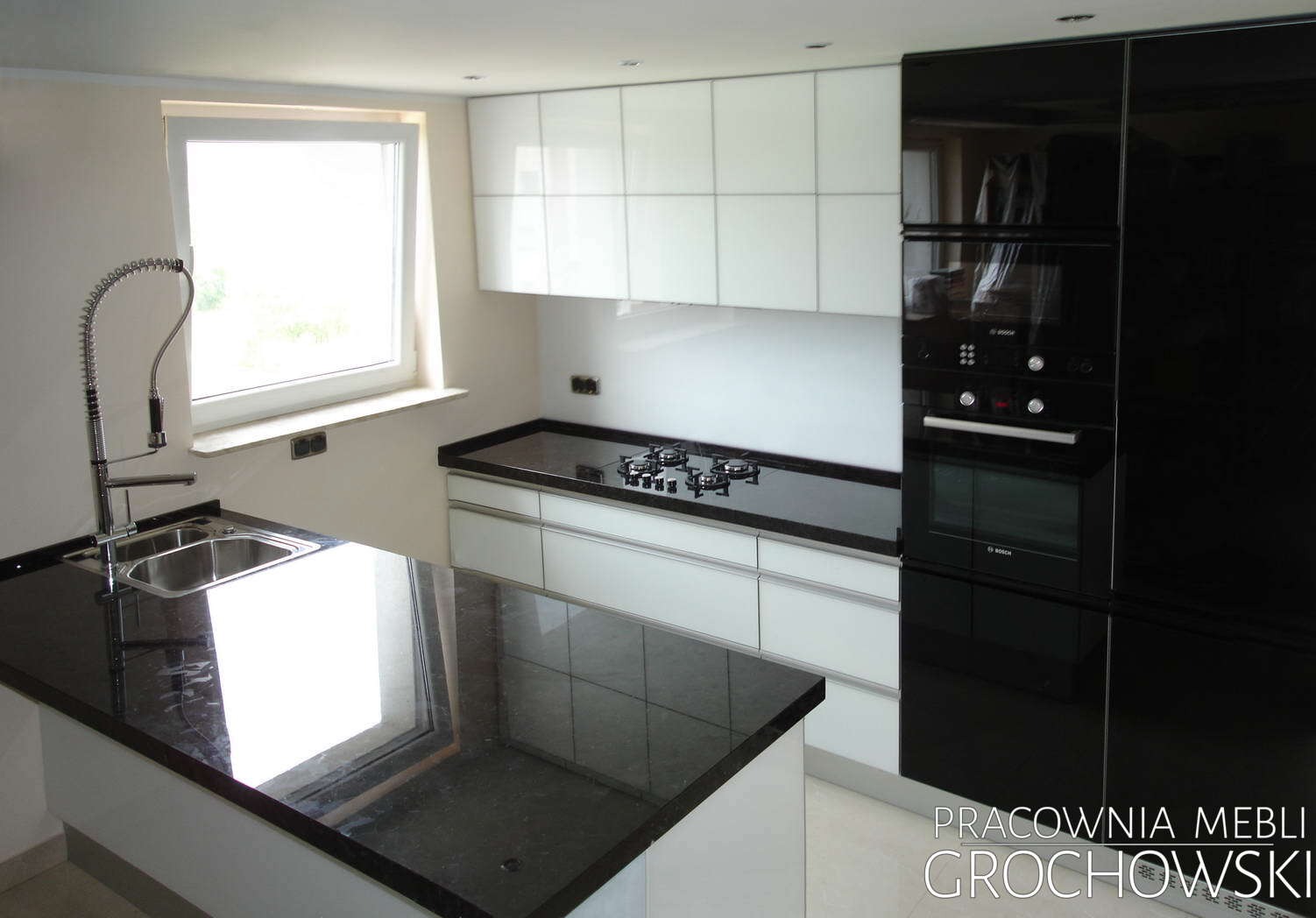 Nowoczesna kuchnia w bieli i czerni z błyszczącymi frontami, czarnym blatem i wyspą, chromowaną baterią z elastyczną wylewką i wbudowanym piekarnikiem.