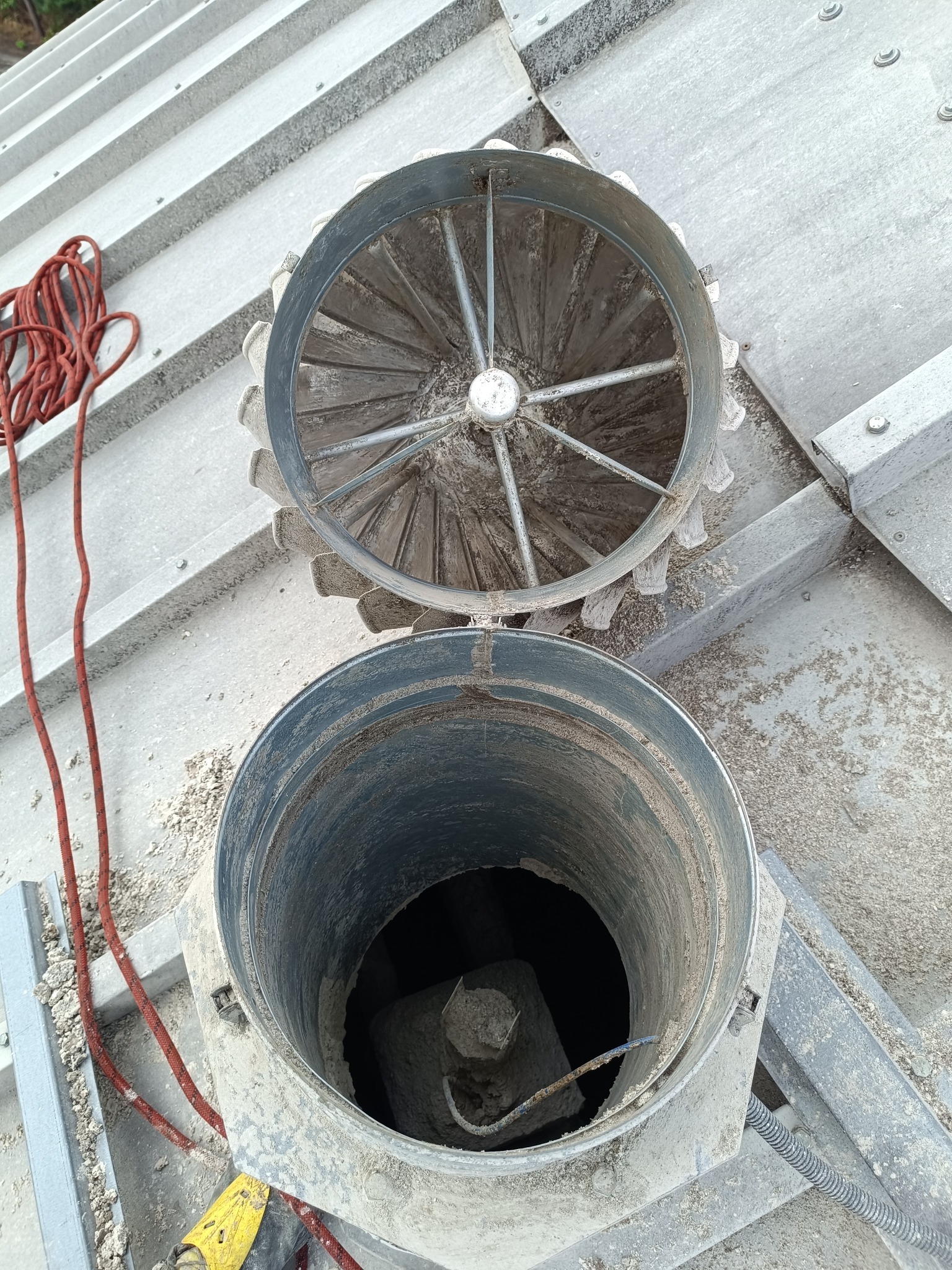 Otwarty, okrągły wentylator na zbiorniku z surowcem sypkim, widoczny z góry. Obok leży czerwona lina. Konstrukcja metalowa, pokryta warstwą pyłu.