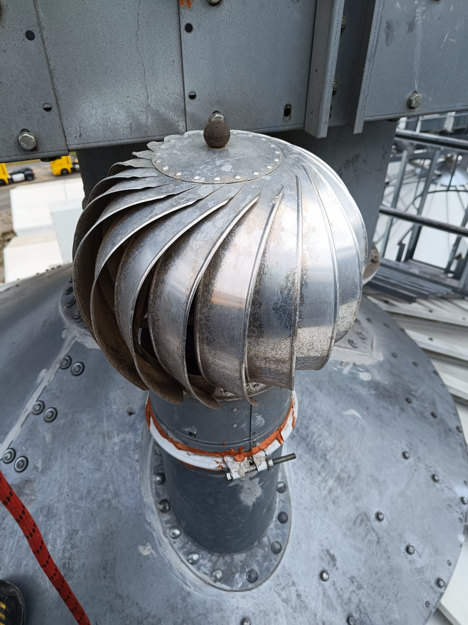 Metalowy wentylator na zbiorniku, widok z góry. Widoczne ślady użytkowania i mocowania śrubowe. Fragment liny asekuracyjnej w lewym dolnym rogu kadru.
