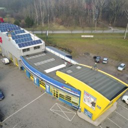 Solaris Oze Sp. z o.o. - Widok z góry na budynek serwisu samochodowego Premio z panelami słonecznymi na dachu, zaparkowane samochody i otaczający teren z drzewami.