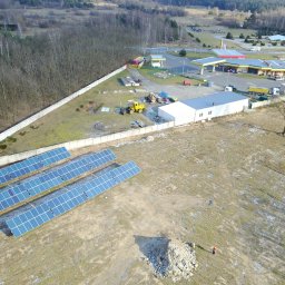 Solaris Oze Sp. z o.o. - Widok z drona na instalację paneli słonecznych na polu, z widoczną stacją benzynową w tle i pracującymi maszynami budowlanymi w pobliżu.
