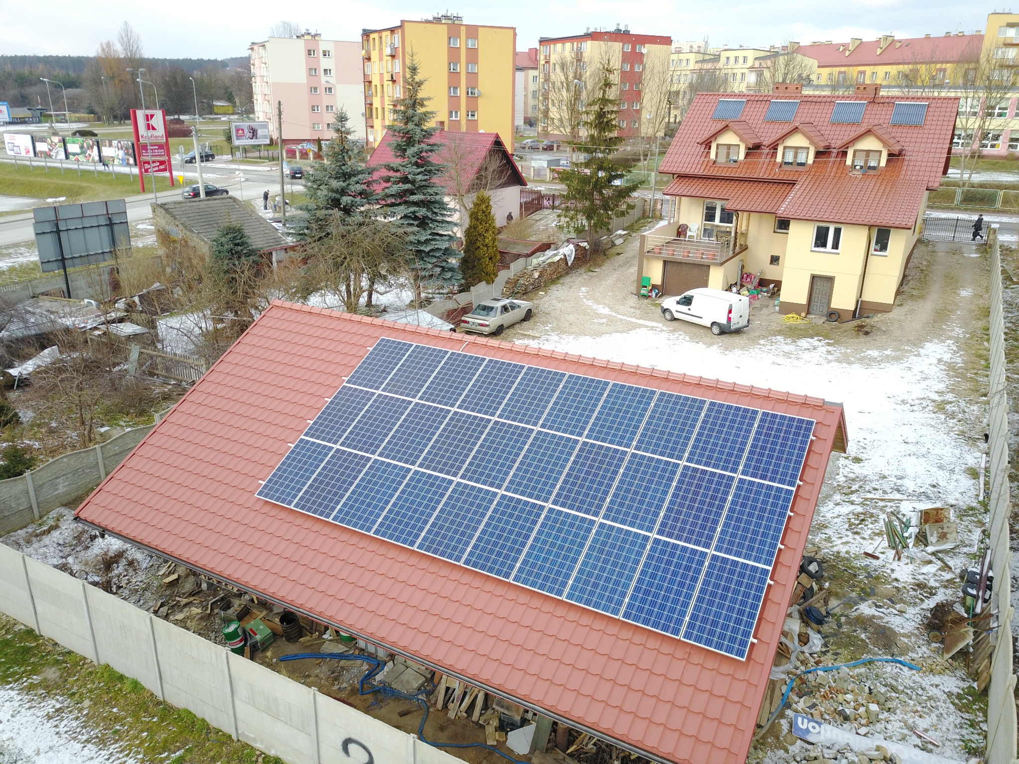 Montaż paneli słonecznych na dachu domu jednorodzinnego w Kielcach, widok z góry na częściowo ośnieżony teren budowy.