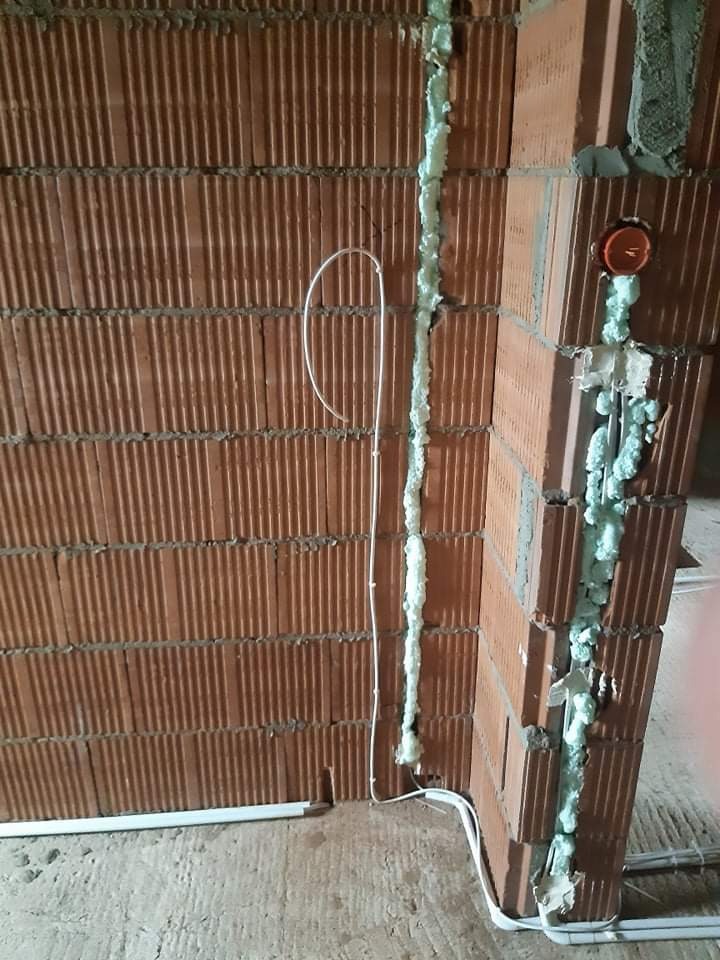 Świeżo wycięte bruzdy w ceglanej ścianie wypełnione pianką montażową, zabezpieczające przewody elektryczne w trakcie instalacji.