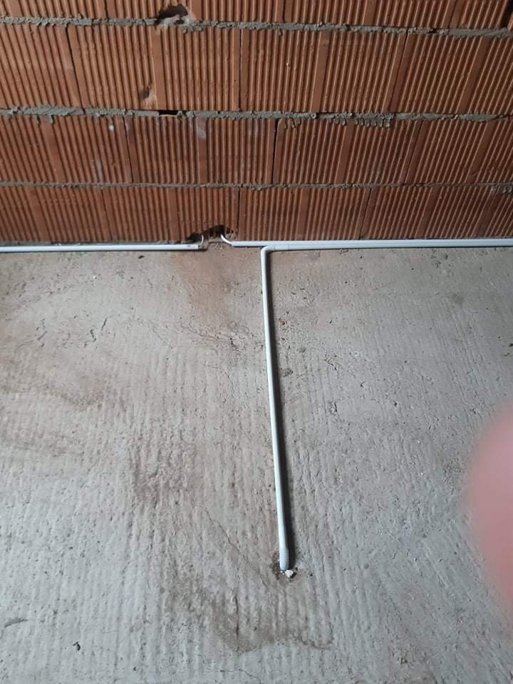 Białe rurki PCV instalacji elektrycznej prowadzone po surowej ścianie z cegły i betonowej podłodze, widoczne mocowania do podłoża.