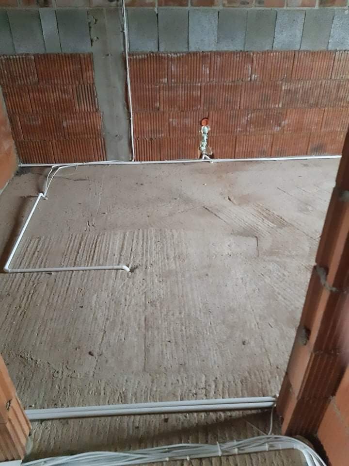 Wnętrze w trakcie remontu z widocznymi przewodami elektrycznymi ułożonymi na podłodze i przymocowanymi do ściany z cegły dziurawki.