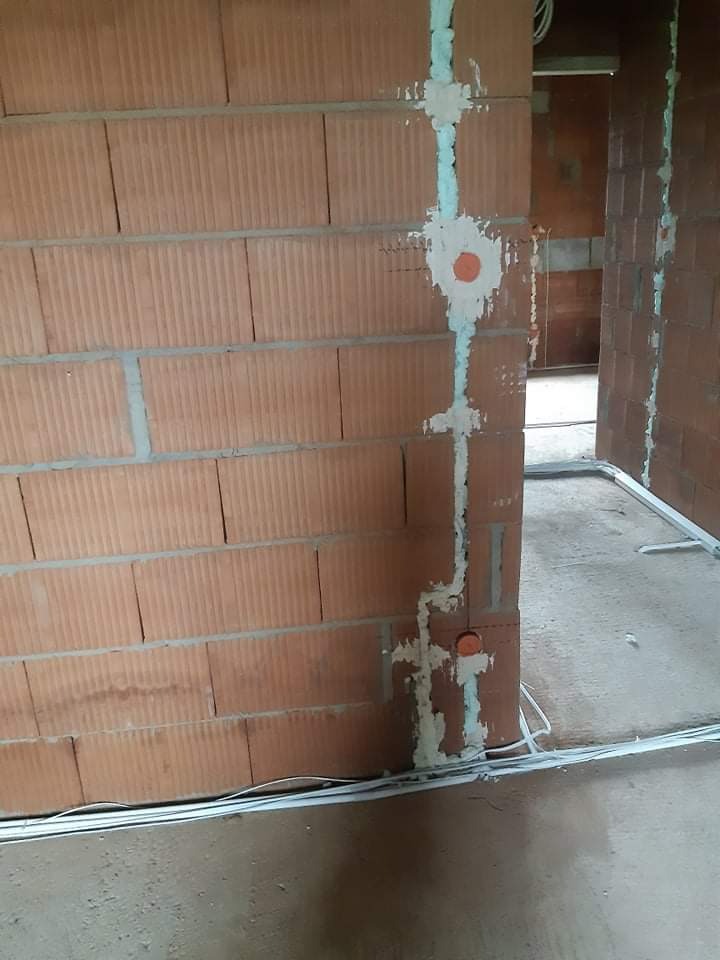 Instalacja elektryczna w trakcie montażu na ścianie z cegły ceramicznej, widoczne kable, puszki instalacyjne i zaprawa gipsowa.