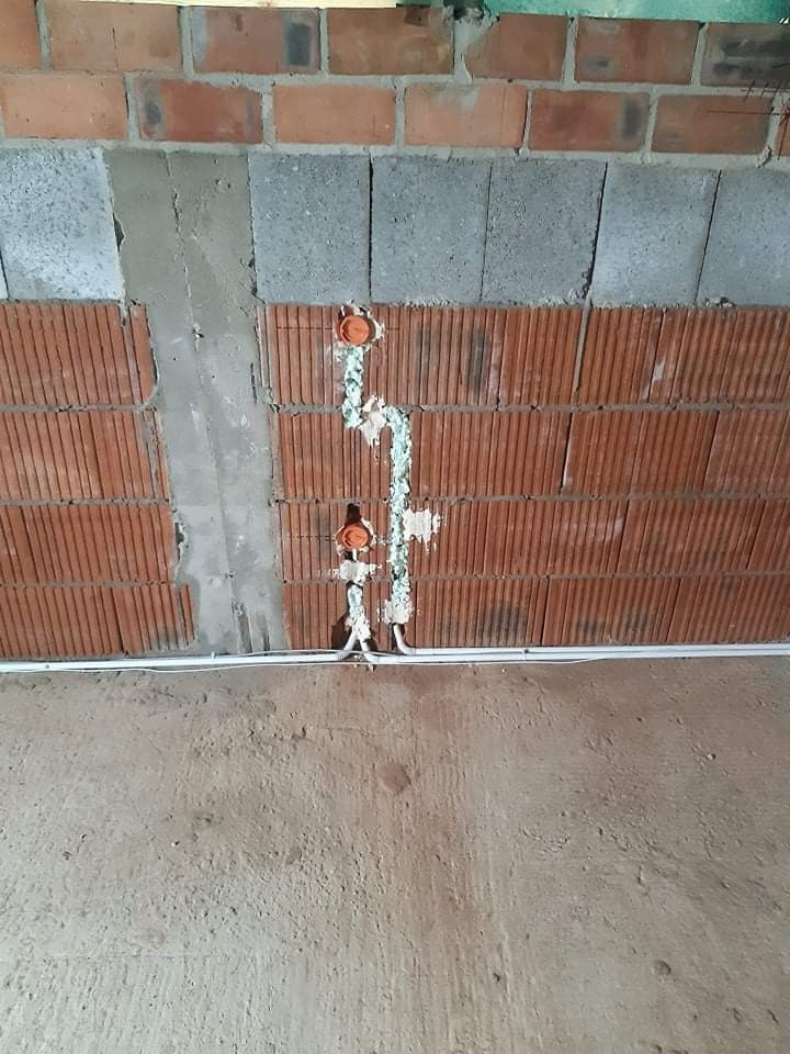 Fragment ściany z cegły dziurawki i bloczków betonowych z wyżłobionymi bruzdami wypełnionymi instalacją elektryczną w peszlach, widoczne puszki instalacyjne pod gniazdka.