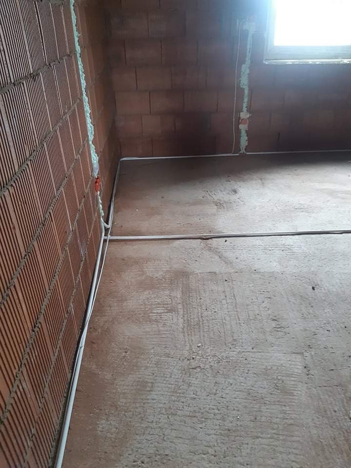 Wnętrze w trakcie prac instalacyjnych: widoczne przewody elektryczne prowadzone wzdłuż ściany z cegły dziurawki, pianka montażowa wokół puszki elektrycznej i okna.