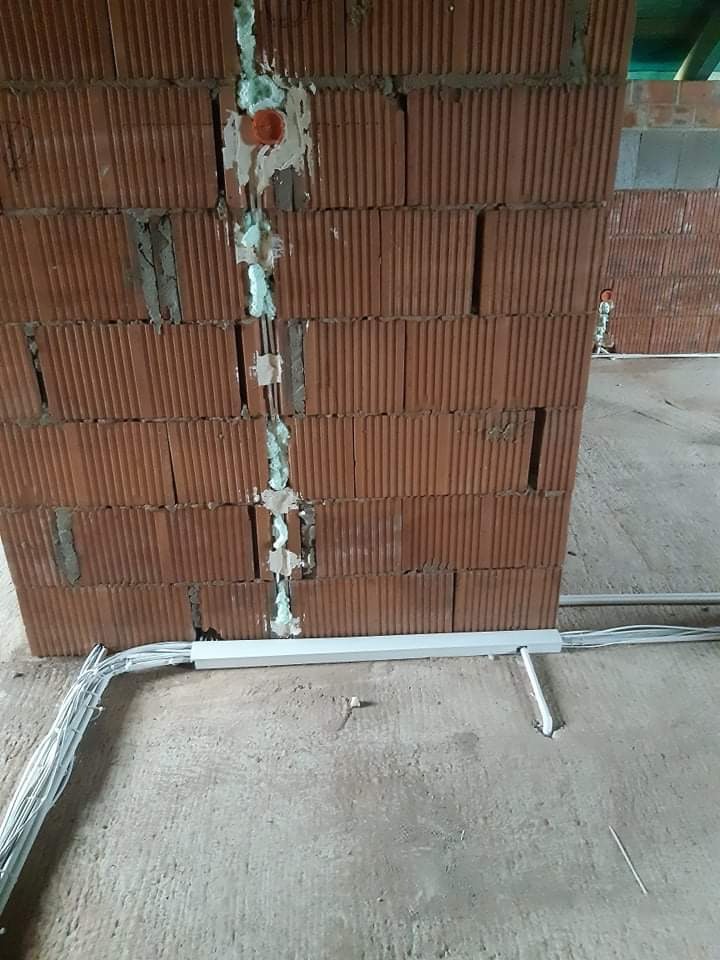 Wewnętrzna ściana z cegły z wyciętymi bruzdami wypełnionymi pianką montażową, w których umieszczono przewody elektryczne i puszkę instalacyjną; przewody prowadzone w listwie przypodłogowej.