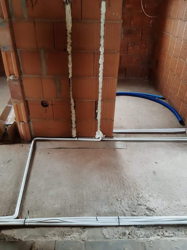 Instalacja przewodów elektrycznych w peszlach i rurkach PCV w surowym wnętrzu z ceglanymi ścianami, zabezpieczonych pianką montażową.