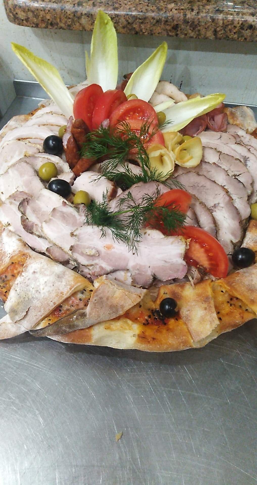 Dekoracyjnie ułożona taca z plastrami pieczonego mięsa, tortellini, pomidorami, oliwkami i endywią na bazie z pieczywa.