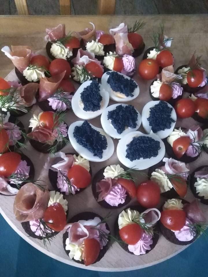 Różnorodne przekąski na drewnianej tacy: jajka z czarnym kawiorem, mini tartaletki z kremem, szynką parmeńską i pomidorkami koktajlowymi, udekorowane koperkiem.