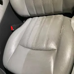 Szare skórzane siedzenie samochodowe z widoczną różnicą w czystości po lewej stronie i uszkodzeniami po prawej, usługa wykonana we Wrocławiu.