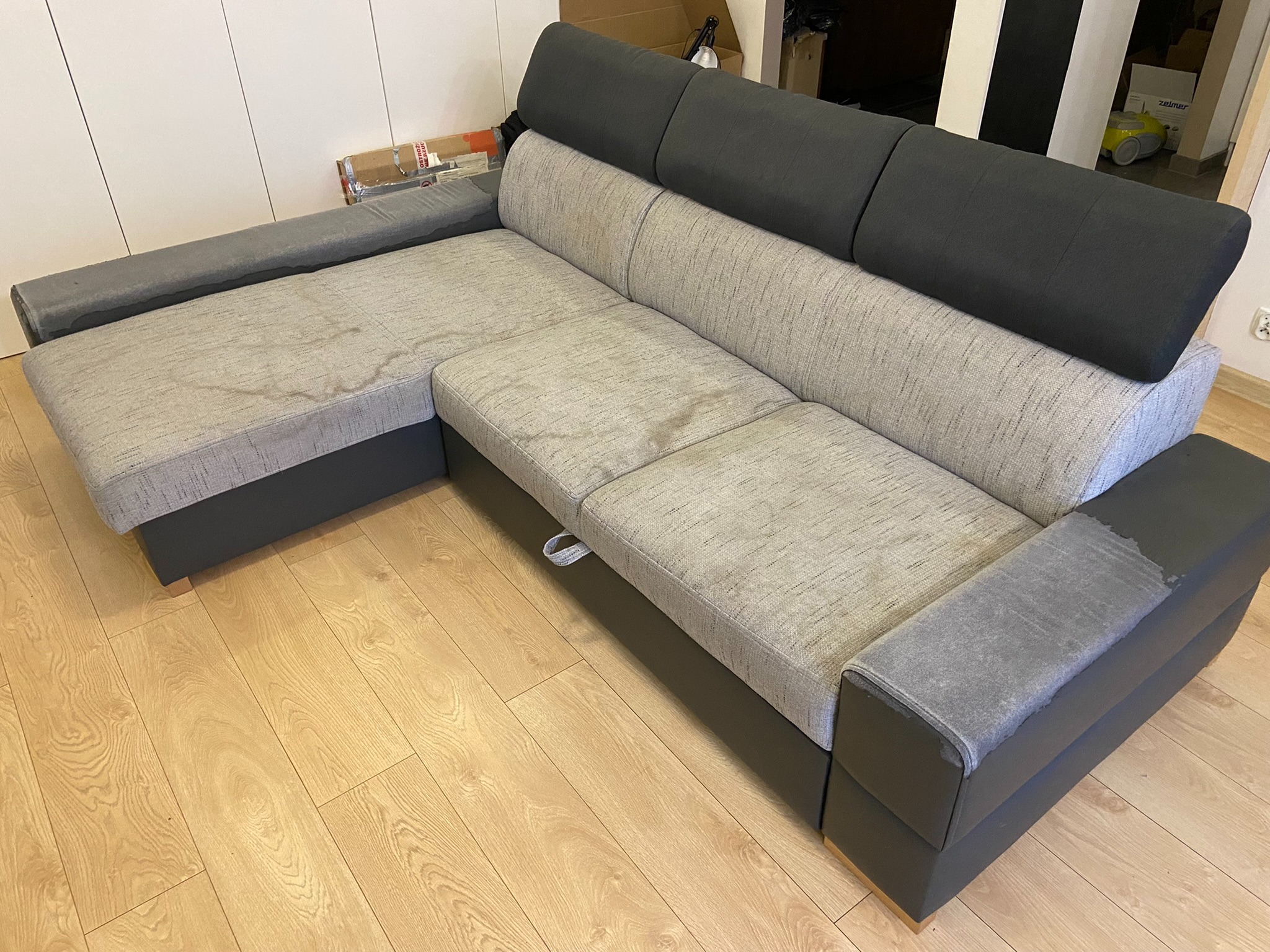 Narożnik z szarą tapicerką z widocznymi plamami na siedzisku, sfotografowany we Wrocławiu, oczekujący na profesjonalne czyszczenie.