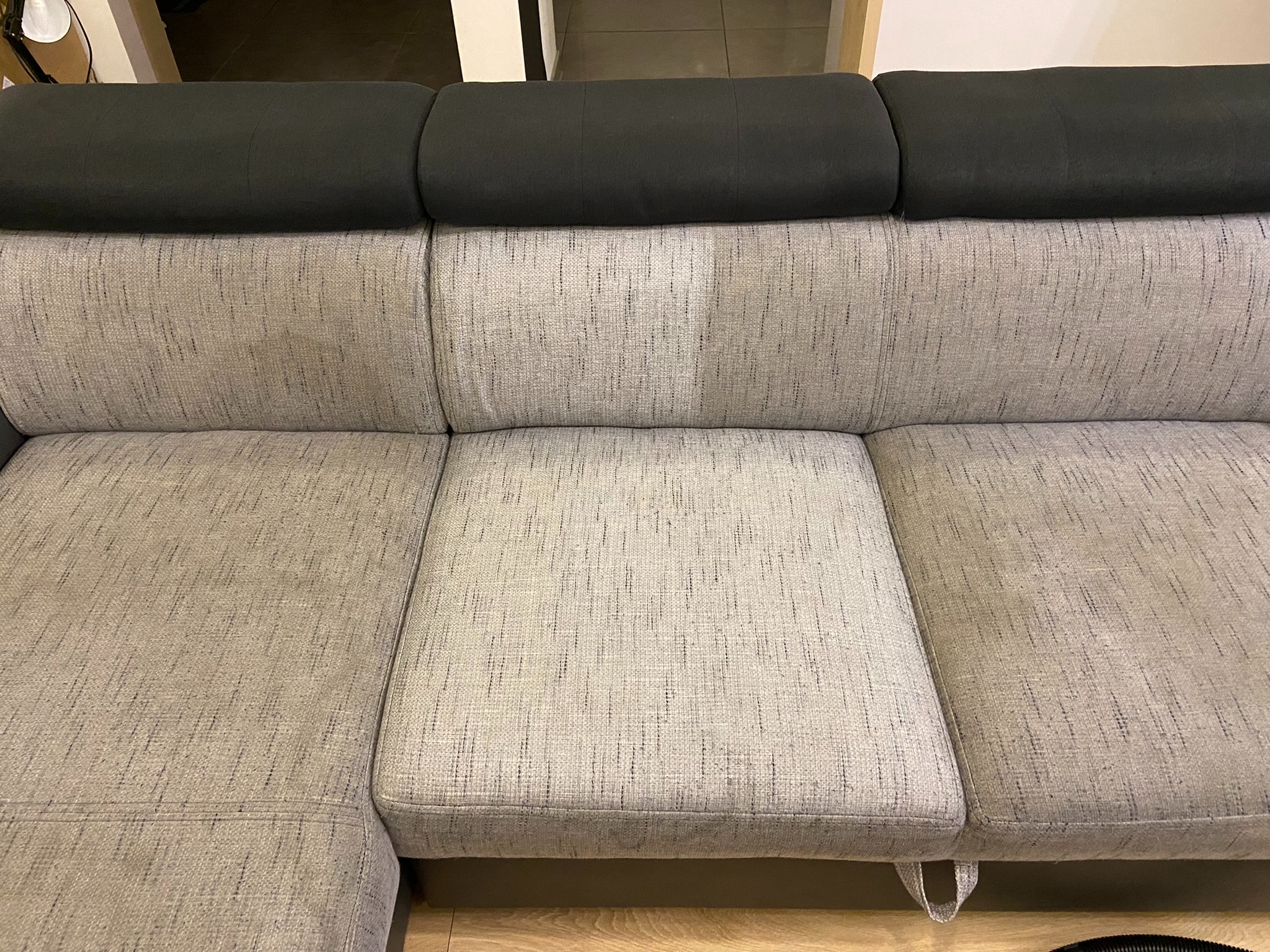 Fragment szarej sofy z czarnym zagłówkiem, widoczny efekt czyszczenia na jednym z siedzisk.