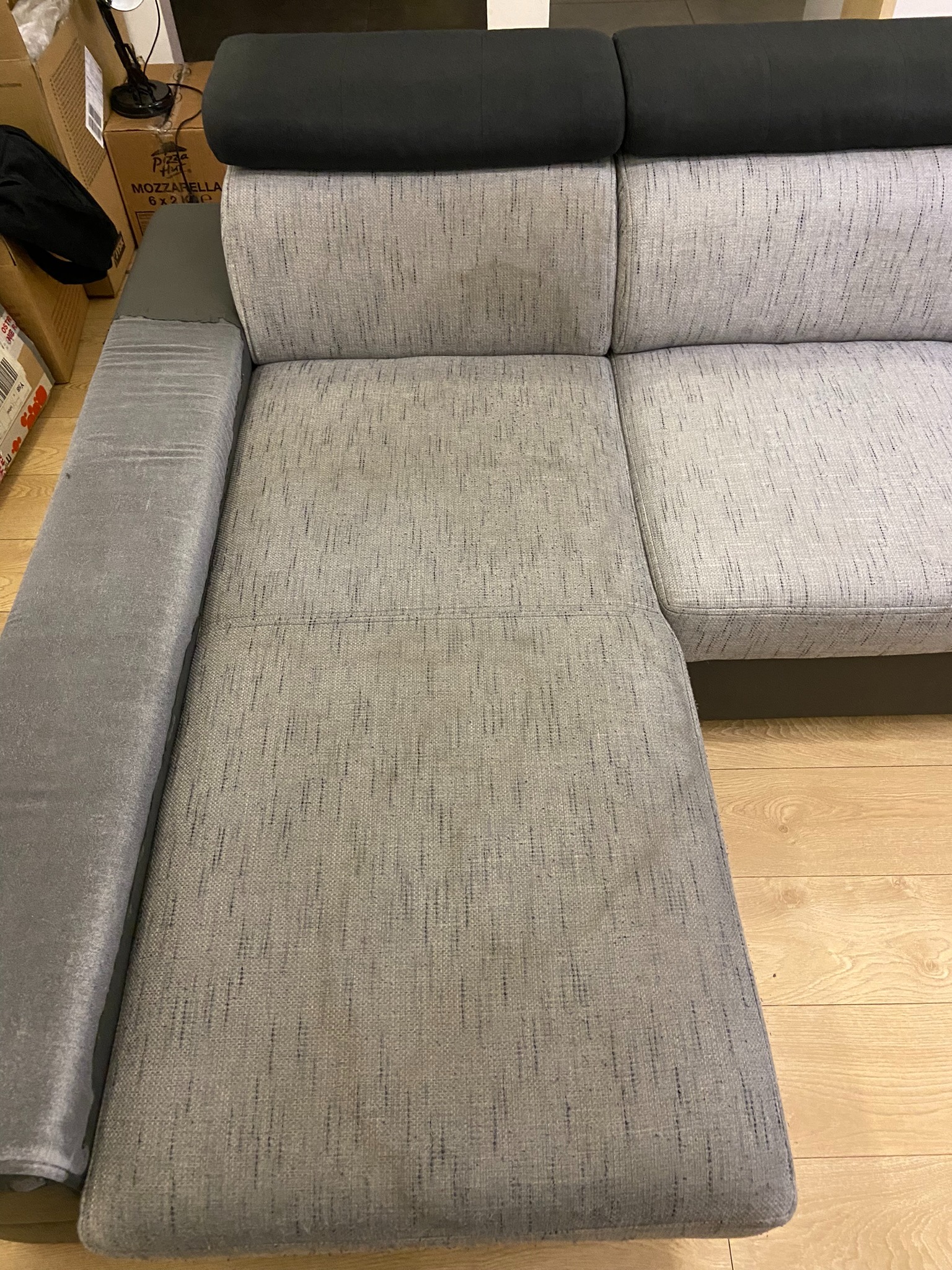 Szary narożnik z ciemnoszarymi zagłówkami, widoczna tekstura materiału i drewniana podłoga w tle.