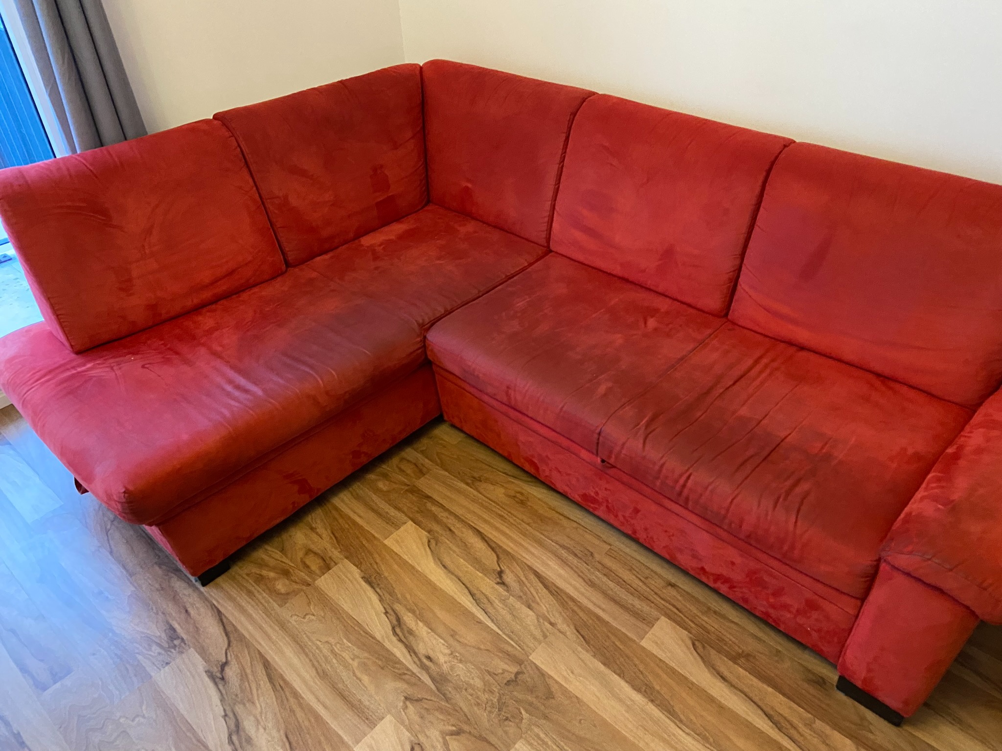 Czerwony narożnik tapicerowany z widocznymi plamami na siedziskach i oparciach, ustawiony na drewnianej podłodze.