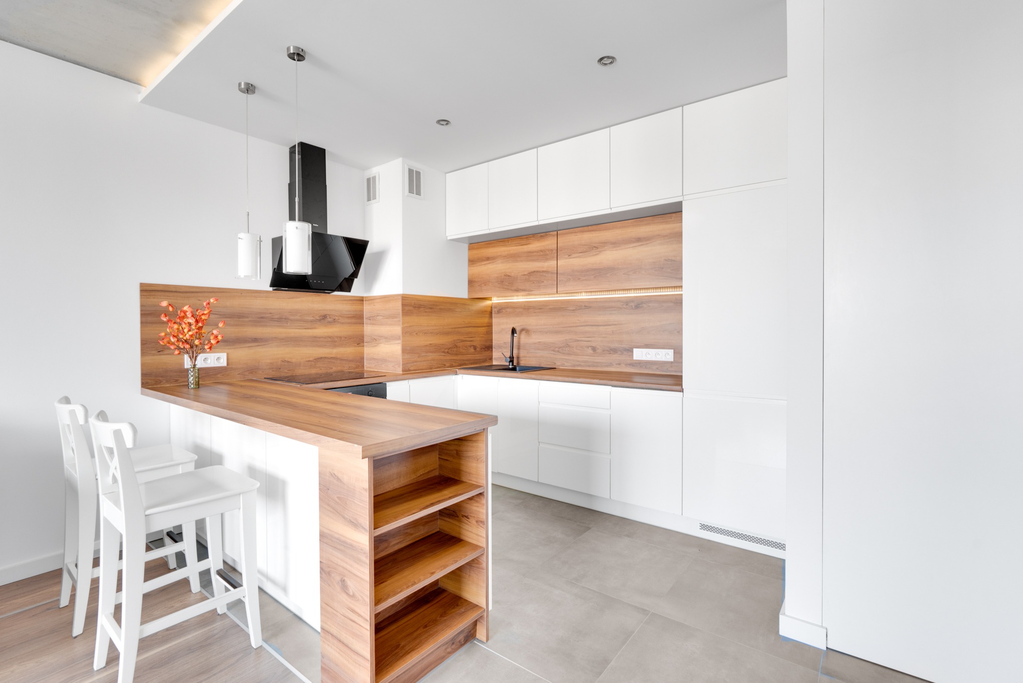Nowoczesna kuchnia z białymi szafkami i drewnianym blatem. Minimalistyczny design z wyspą i hokerami, oświetlenie punktowe. Aranżacja wnętrza.