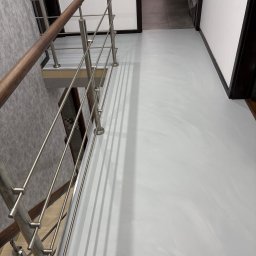 BW Floor Ewa Wołowicz - Jasnoszara, gładka posadzka żywiczna w korytarzu, widok z góry na schody z metalową balustradą i drewnianym poręczą. Minimalistyczne wnętrze z białymi ścianami.