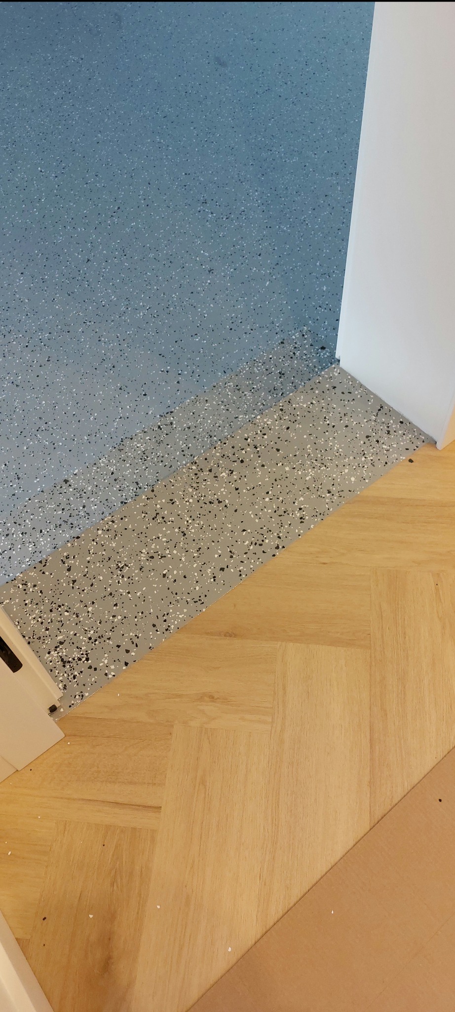 Połączenie dwóch typów podłóg: żywicznej w odcieniach szarości i drewnianej ułożonej w jodełkę w Bieniewicach. Widoczne przejście między materiałami.