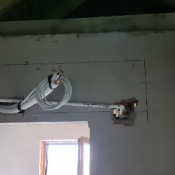 Białe rury instalacji chłodniczej prowadzone po ścianie wewnątrz budynku, widoczne ślady po wykuwaniu otworów, zaznaczone ołówkiem wymiary montażowe, surowy stan wykończenia pomieszczenia.