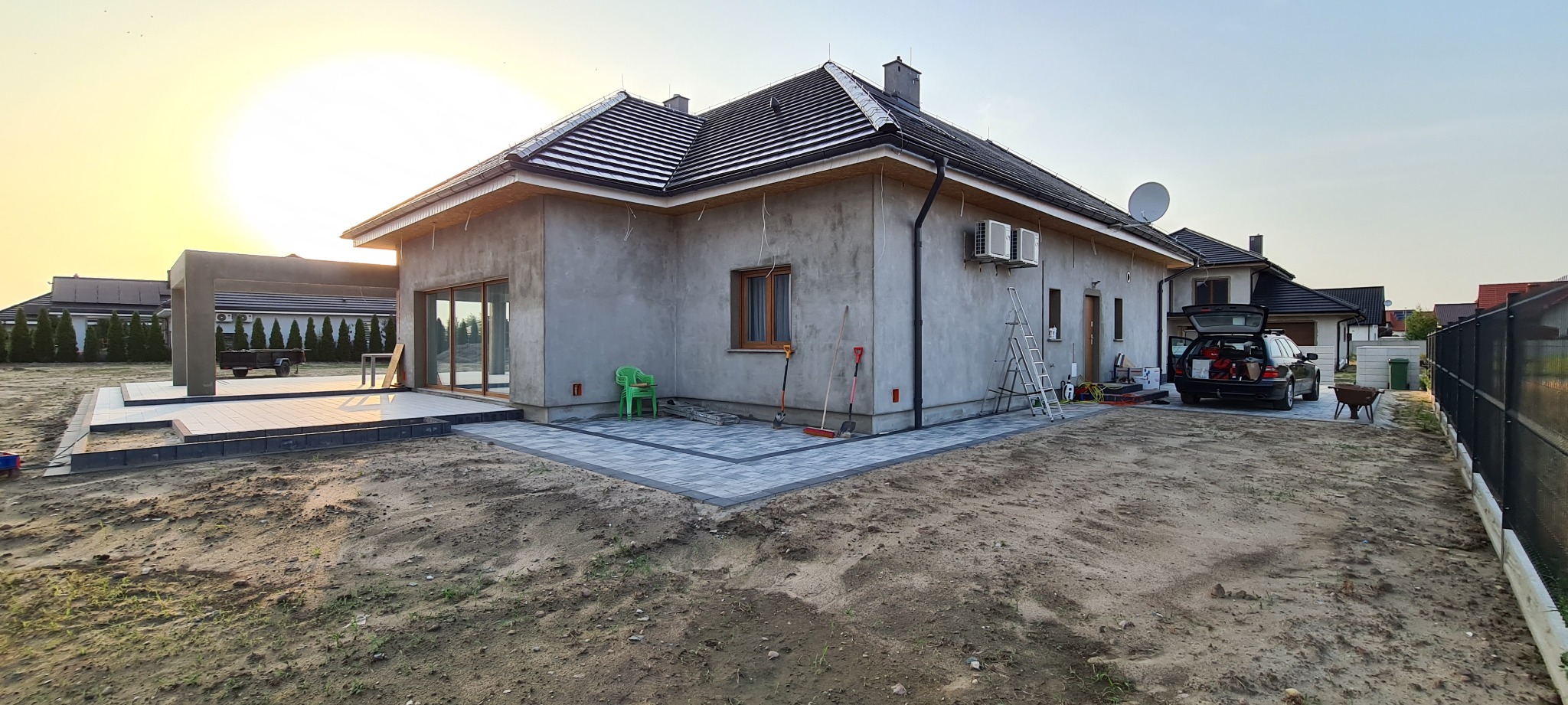 Dom jednorodzinny w trakcie wykończenia z zamontowanymi dwoma klimatyzatorami na elewacji, widoczne narzędzia i drabina, świeżo ułożona kostka brukowa wokół budynku.