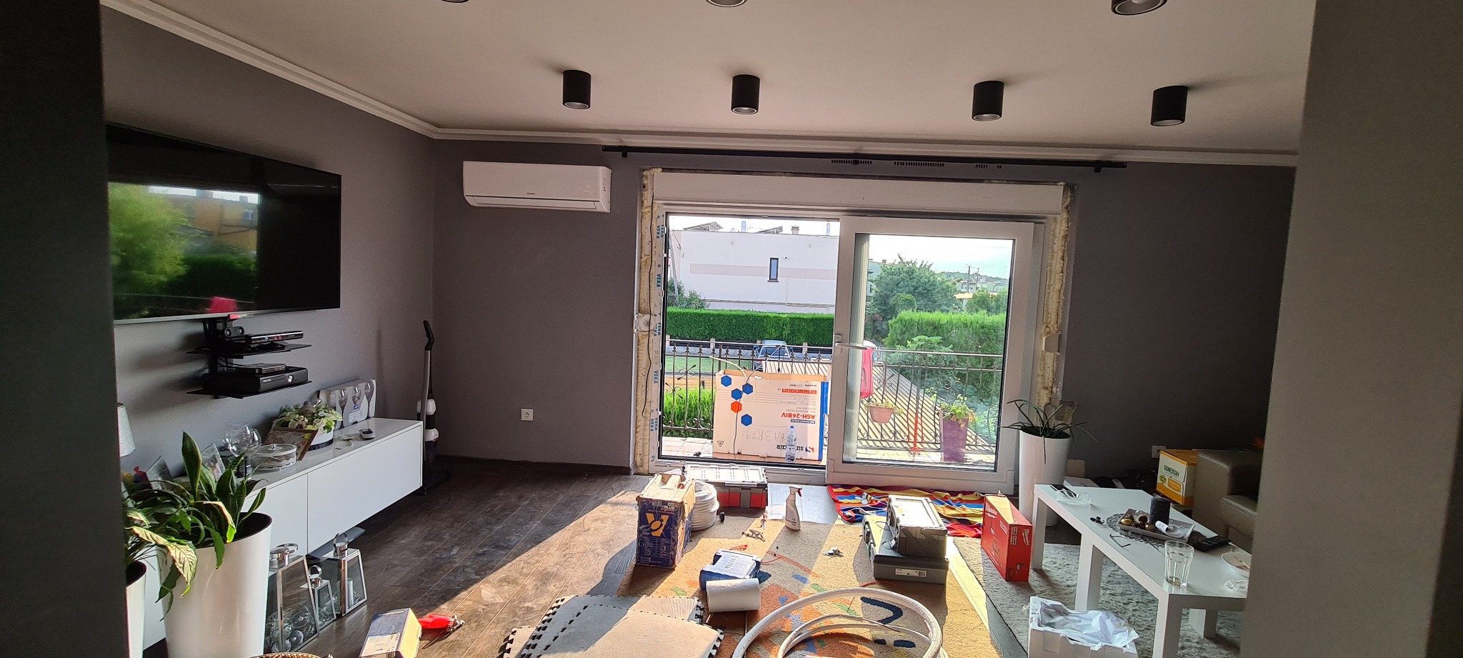 Wnętrze mieszkania w trakcie montażu klimatyzacji, widoczny klimatyzator na ścianie, otwarte drzwi balkonowe z pianką montażową wokół ościeżnicy i narzędzia pracy na podłodze.