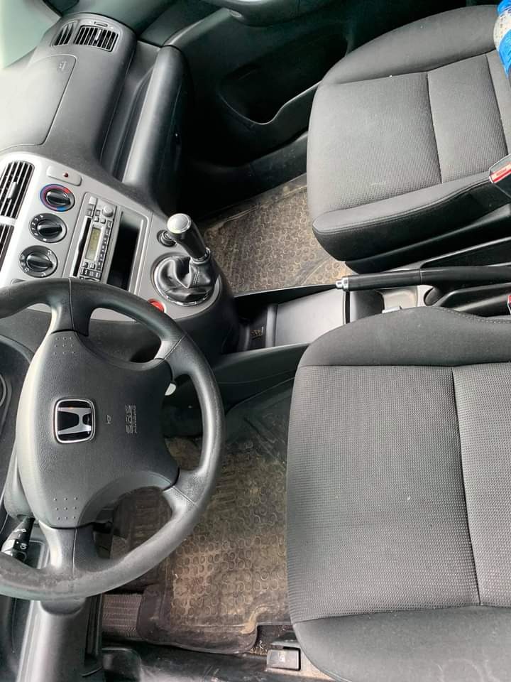 Wnętrze samochodu marki Honda Civic, widoczne przednie fotele z szarej tapicerki, kierownica z logo producenta, deska rozdzielcza z radiem, oraz gumowe dywaniki z widocznymi zabrudzeniami.