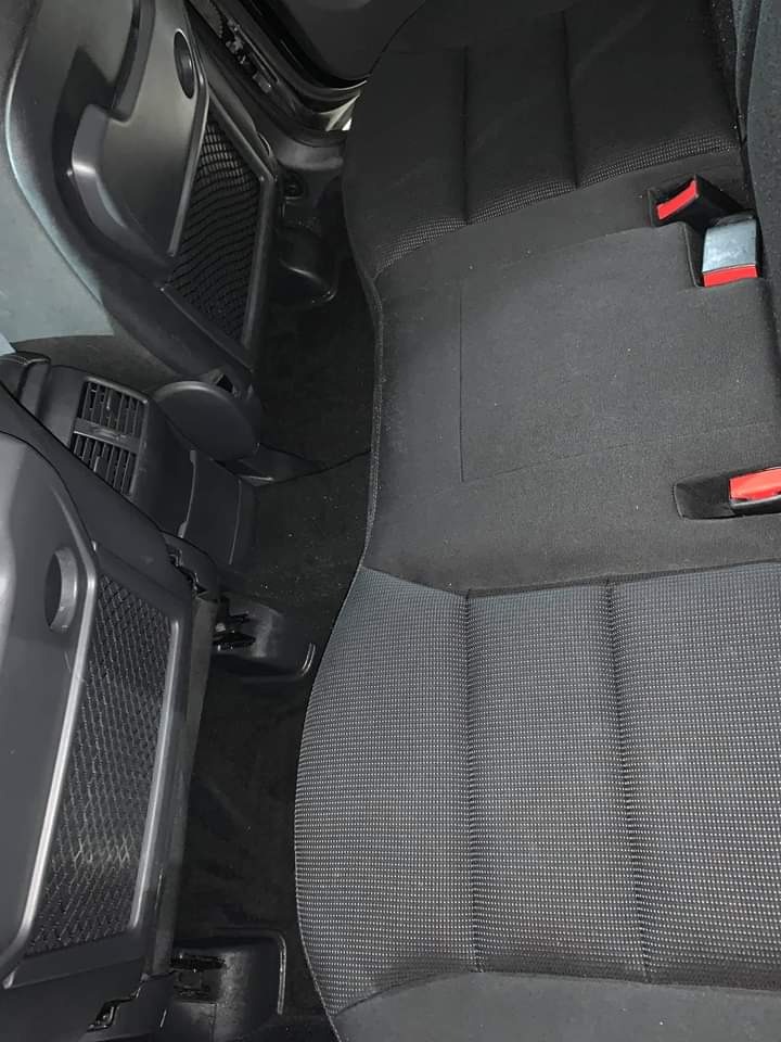 Wnętrze samochodu, tylna kanapa z ciemną tapicerką w kratkę, widoczne zagłówki, pasy bezpieczeństwa z czerwonymi elementami oraz kieszeń w bocznej części obicia.