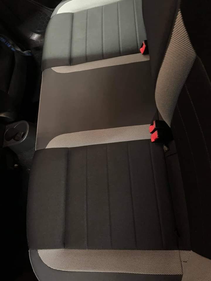 Wnętrze samochodu z widoczną tylną kanapą z czarno-szarą tapicerką i czerwonymi elementami zapięć pasów bezpieczeństwa.