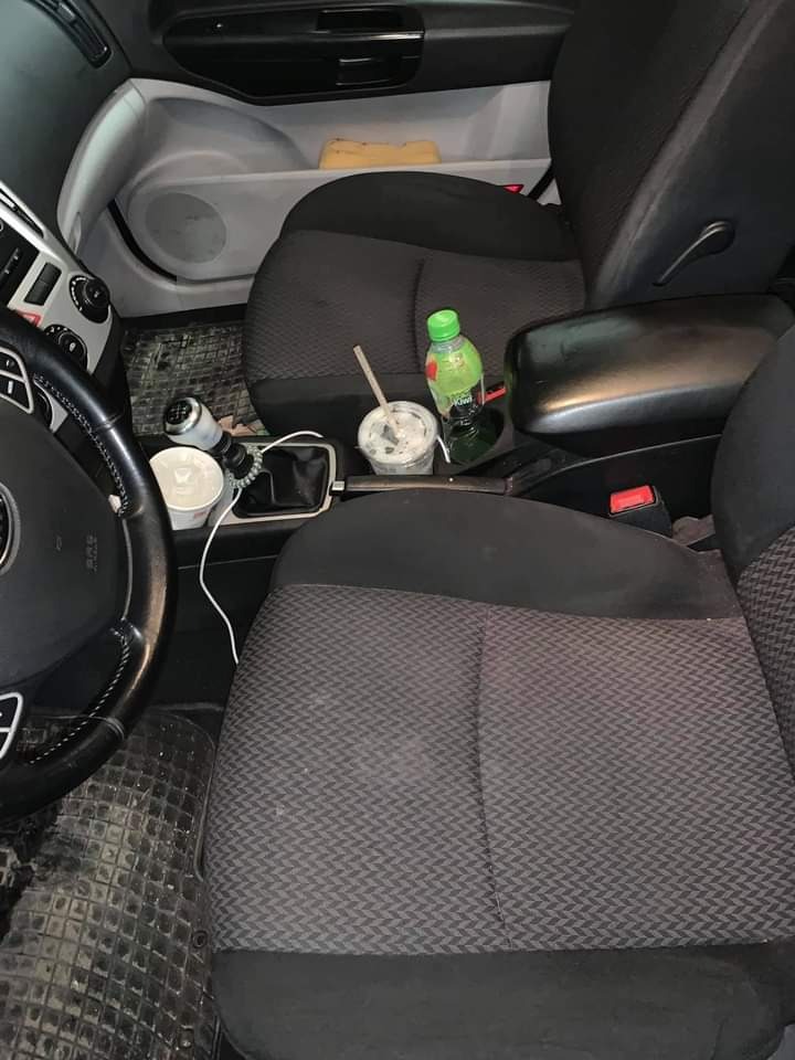 Wnętrze samochodu z widocznymi zabrudzeniami na fotelach, podłodze i konsoli środkowej, napój i kubek z resztkami na podłokietniku.