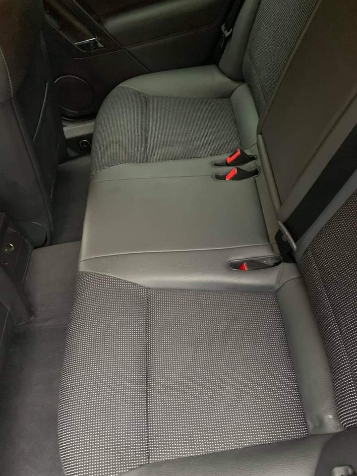 Wnętrze samochodu z tylną kanapą o szarej, teksturowanej tapicerce, widoczne czerwone zatrzaski pasów bezpieczeństwa.