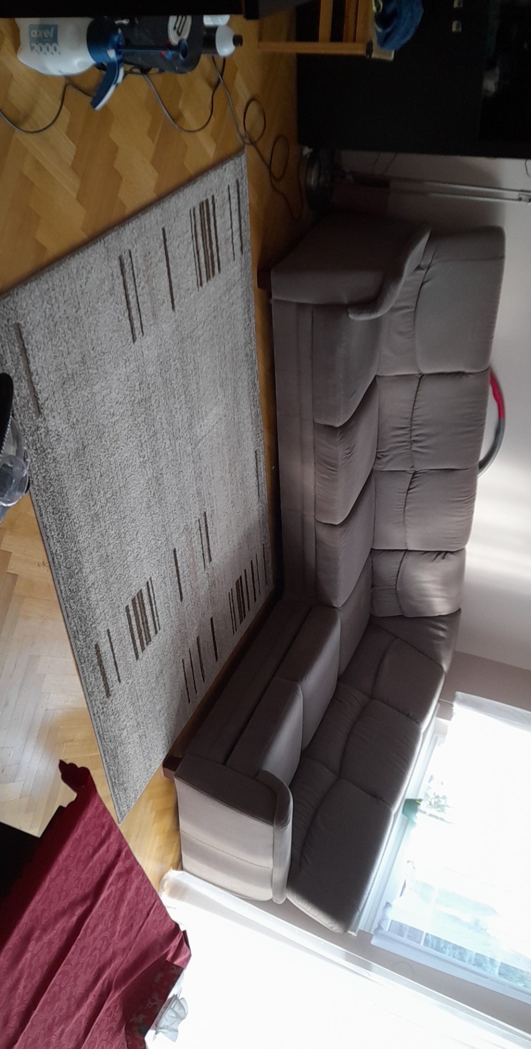 Szara, modułowa sofa tapicerowana obok dywanu w paski, widoczny odkurzacz Axel 2000 na parkiecie.