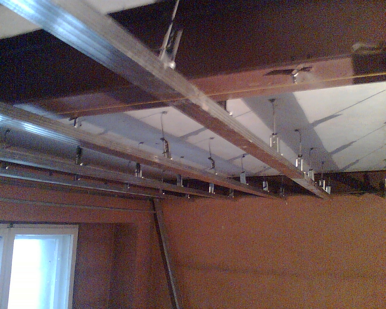 Stelaż metalowy sufitu podwieszanego w trakcie montażu, widoczne profile i elementy mocujące do stropu, ściana w tle z oknem.