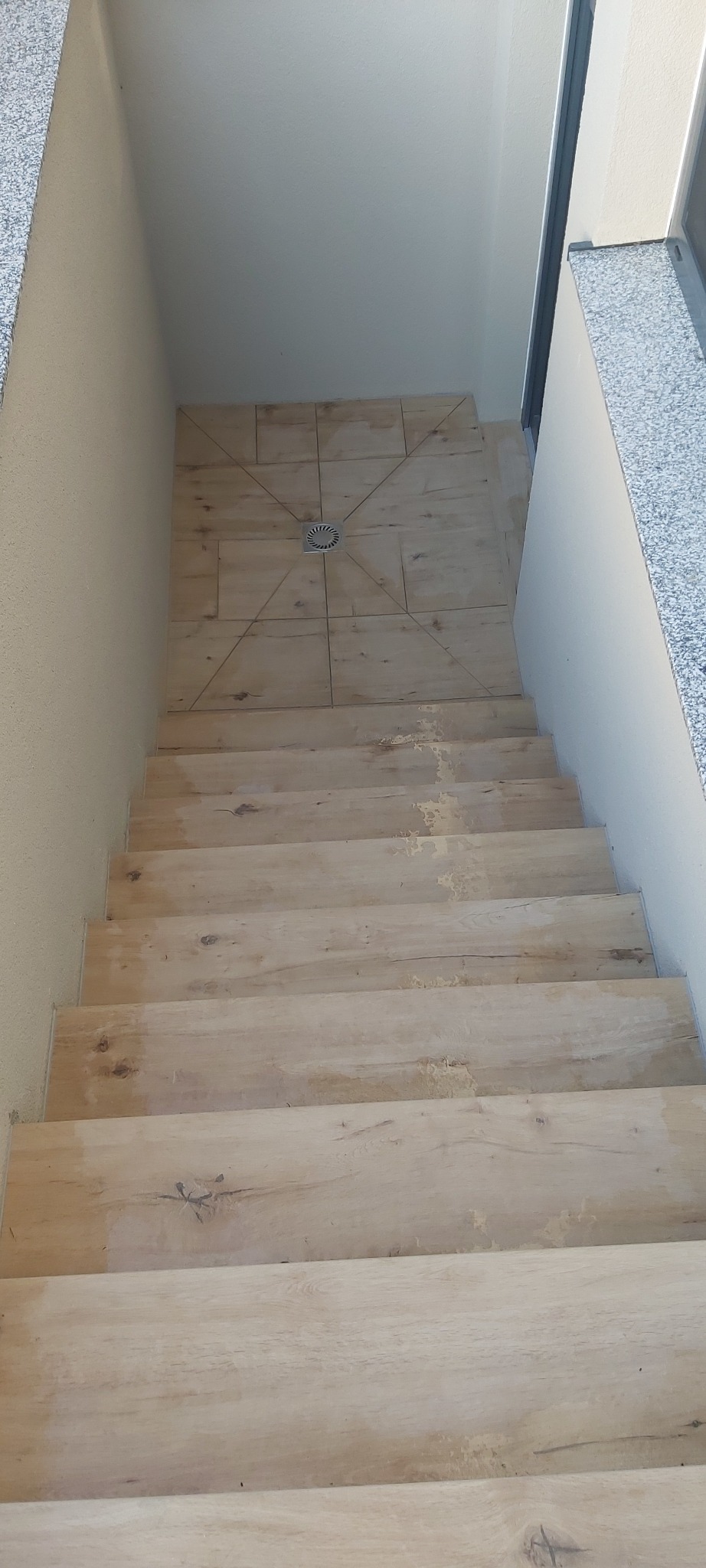 Schody wyłożone płytkami imitującymi drewno, z odpływem liniowym na górnym podeście, widok z góry w trakcie montażu.