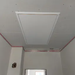 Sufit podwieszany z płyt gipsowo-kartonowych z zamontowaną klapą rewizyjną, widoczne czerwone przewody elektryczne wzdłuż ścian oraz otwór na gniazdko elektryczne.