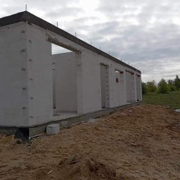 Zakład Ogólnobudowlany Jakub Szymkowiak - Surowy stan domu z betonu komórkowego z widocznymi otworami okiennymi i drzwiowymi, na etapie wznoszenia ścian, z ziemią i zielenią w tle pod pochmurnym niebem.