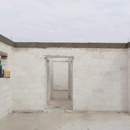 Zakład Ogólnobudowlany Jakub Szymkowiak - Wnętrze surowego, parterowego domu w trakcie budowy, ściany z białych bloczków, widoczne otwory okienne i drzwiowe, na parapecie poziomica laserowa.