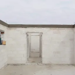 Wnętrze surowego, parterowego domu w trakcie budowy, ściany z białych bloczków, widoczne otwory okienne i drzwiowe, na parapecie poziomica laserowa.