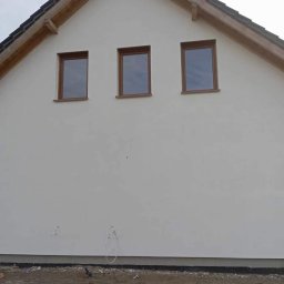 Zakład Ogólnobudowlany Jakub Szymkowiak - Boczny widok na nowo otynkowany dom z trzema oknami w drewnianych ramach, widoczne wystające kable i fragment gruntu.