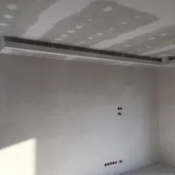 Wnętrze w trakcie szpachlowania: sufit z widocznymi łączeniami płyt gipsowo-kartonowych, ściana z przygotowanymi otworami na gniazdka elektryczne, listwa dekoracyjna pod sufitem.