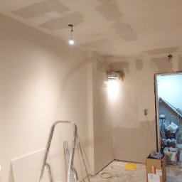 BART-BUD - Wnętrze w trakcie remontu: ściany przygotowane do malowania, widoczne ślady po szpachlowaniu na suficie i ścianach, drabina malarska, niezabezpieczona instalacja elektryczna, bałagan w tle.