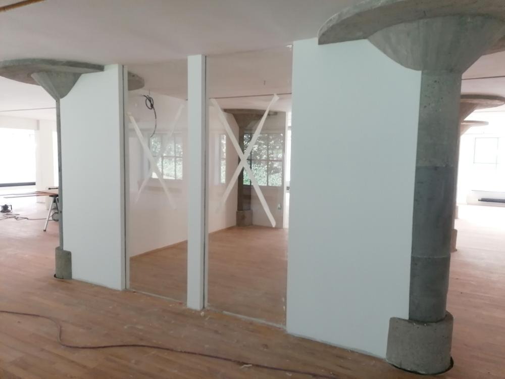 Montaż ścianek działowych z płyt kartonowo-gipsowych w biurze, widoczne surowe, betonowe kolumny i drewniana podłoga w trakcie prac.