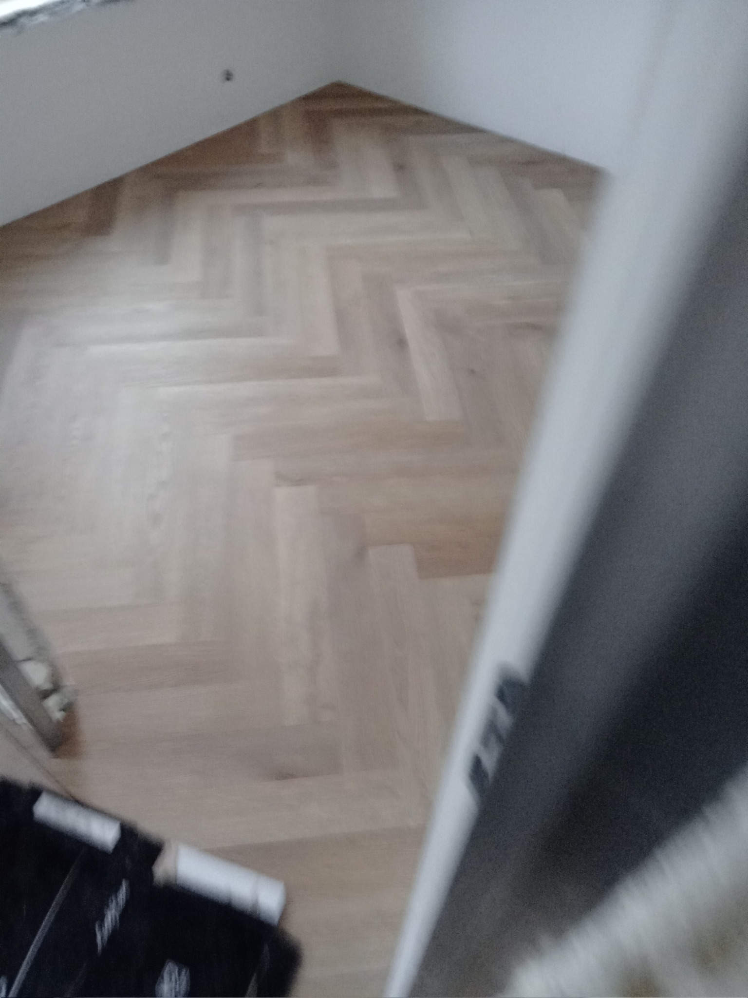 Jasny parkiet ułożony we wzór jodełki francuskiej w pokoju na poddaszu, widoczny fragment czarnej skrzynki narzędziowej w rogu.