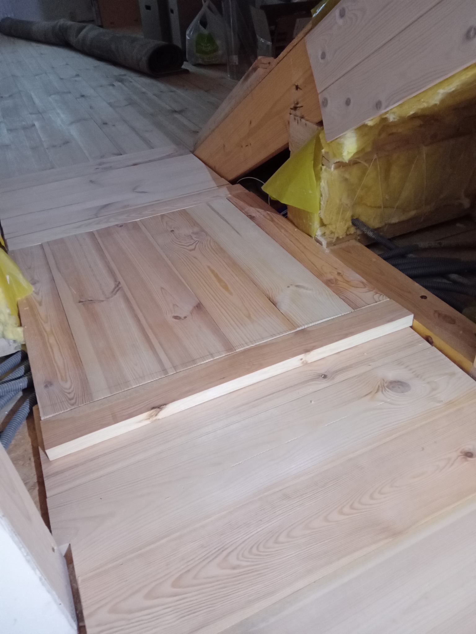 Fragment podłogi na poddaszu z jasnych, surowych desek, widoczne ocieplenie żółtą wełną mineralną i fragment instalacji elektrycznej w peszlu.