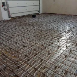 Montaż ogrzewania podłogowego w hali produkcyjnej z widoczną siatką zbrojeniową i rurami grzewczymi przed wylaniem posadzki.