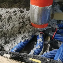 Poddasze z izolacją z wełny mineralnej, widoczne niebieskie rury wentylacyjne i przewody elektryczne w peszlu, zabezpieczone folią kominową.