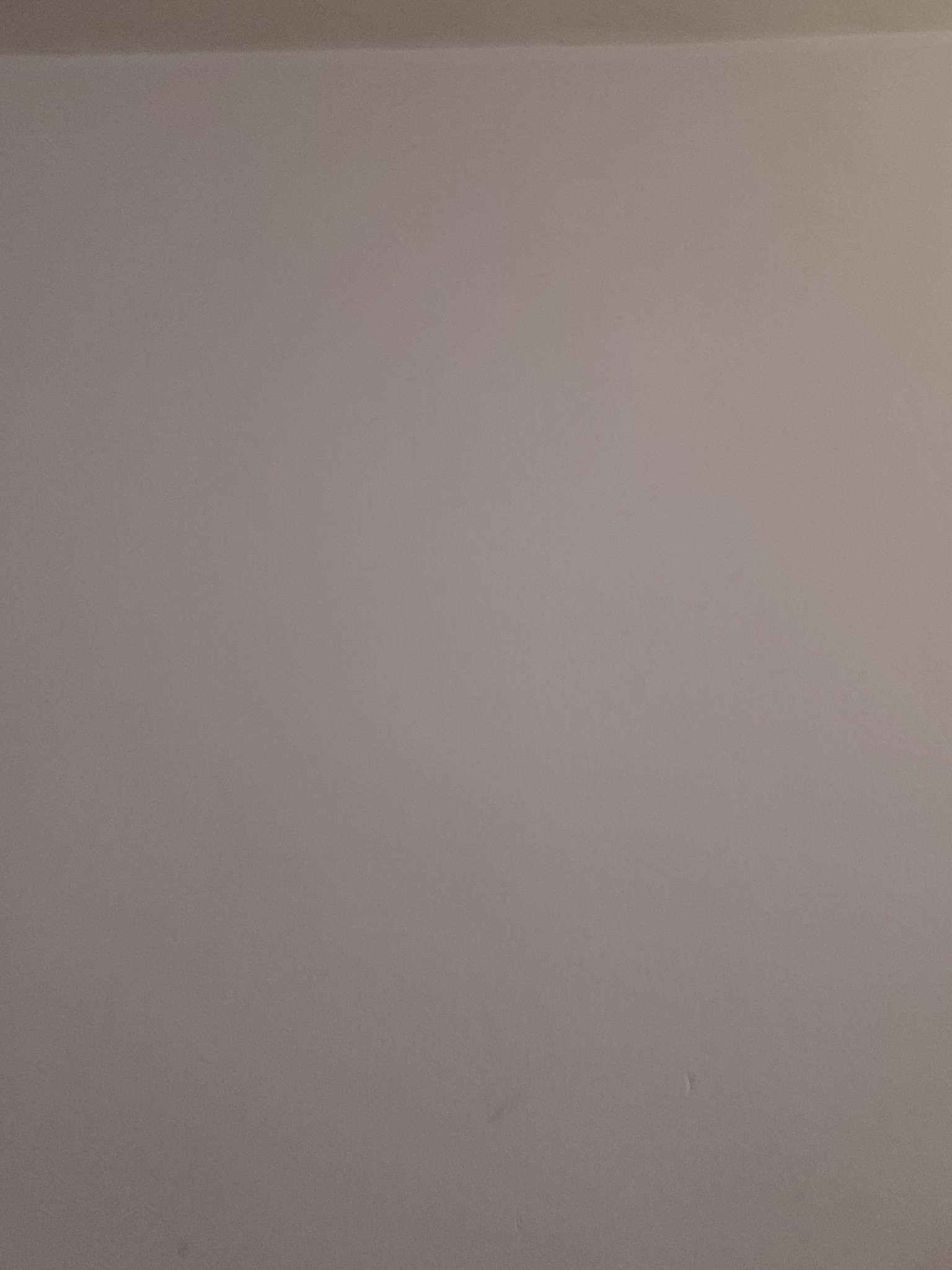 Pusta, jasnoszara ściana z delikatnym załamaniem światła u góry i drobnymi niedoskonałościami w dolnej części.