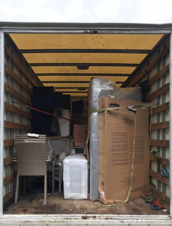 Wnętrze skrzyni ładunkowej wypełnione meblami ogrodowymi, zapakowaną kanapą i kartonami, zabezpieczone pasami transportowymi.